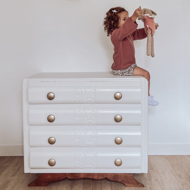 petite fille avec son doudou assise dans sa chambre décorée d'une commode art déco blanche