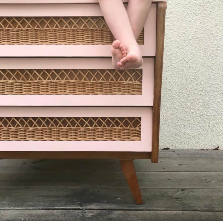 pieds de petite fille devant une commode scandinave rose en rotin et pieds compas