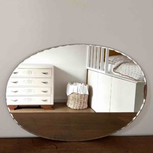 miroir ciselé art déco posé sur un meuble et reflet d'une chambre